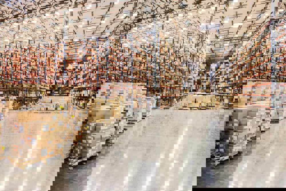 View down aisles of racks holding cardboard boxes of product on pallets in a large distribution warehouse
