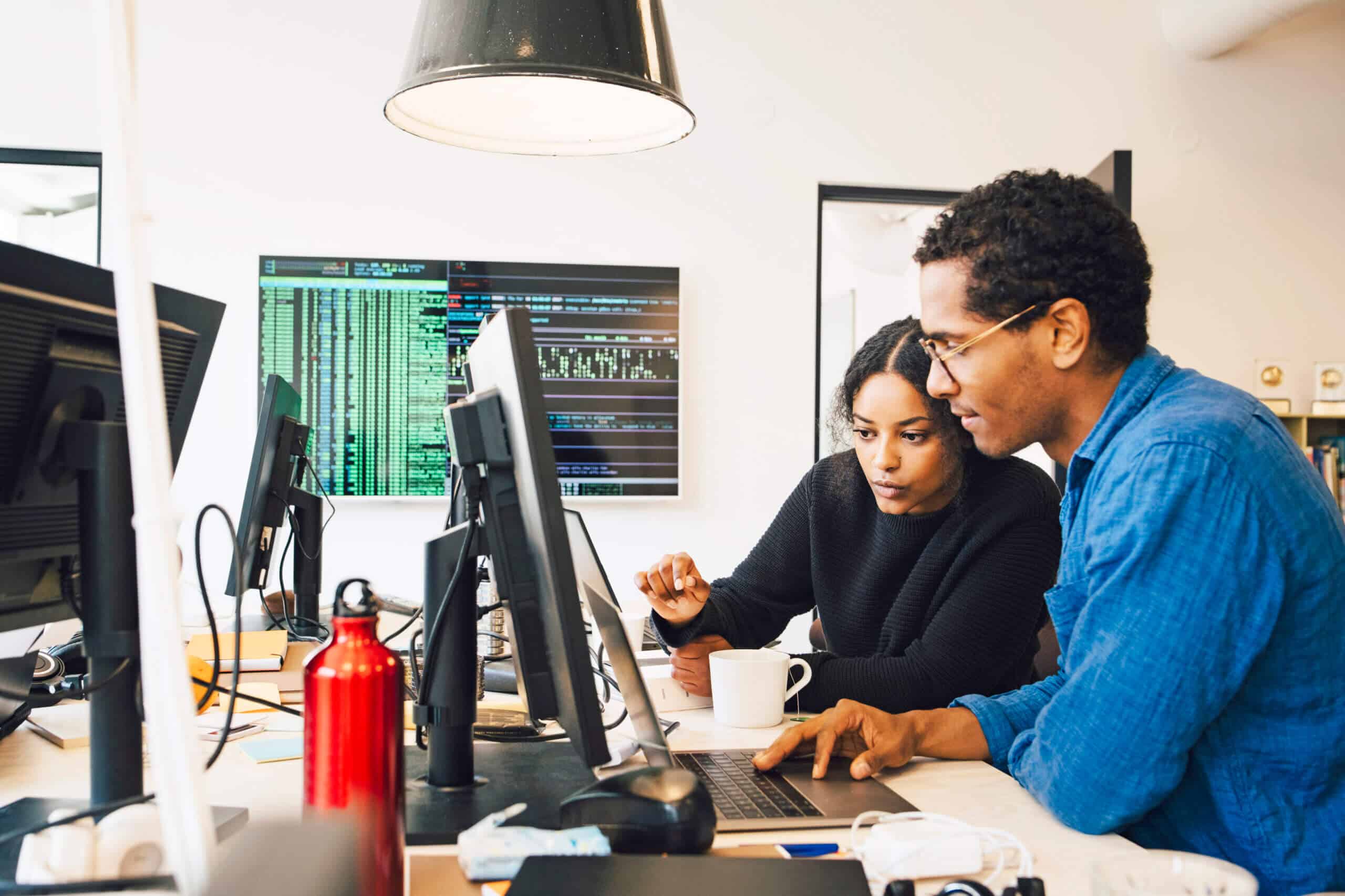 Focused male and female engineers coding over laptop on desk in office