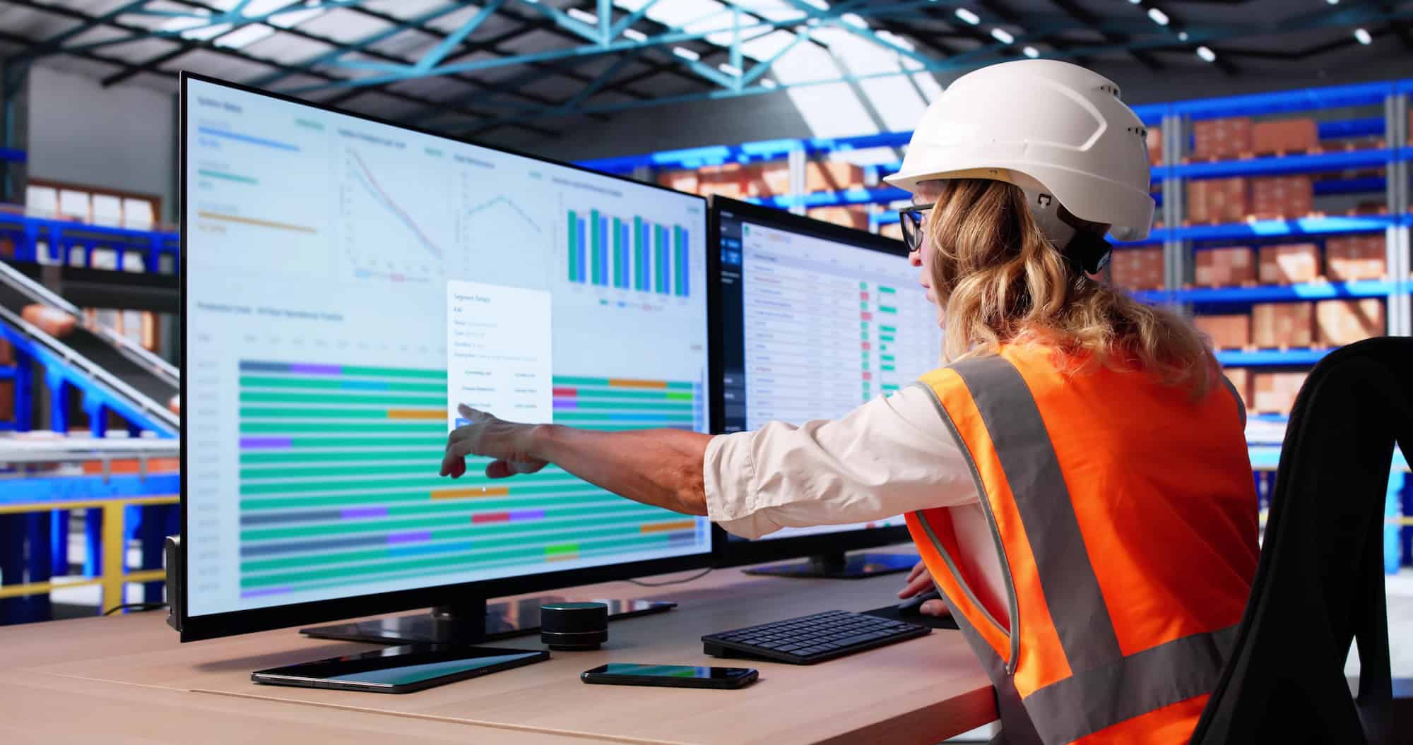 Supply chain manager reviewing real-time control tower dashboards on dual monitors inside a warehouse.