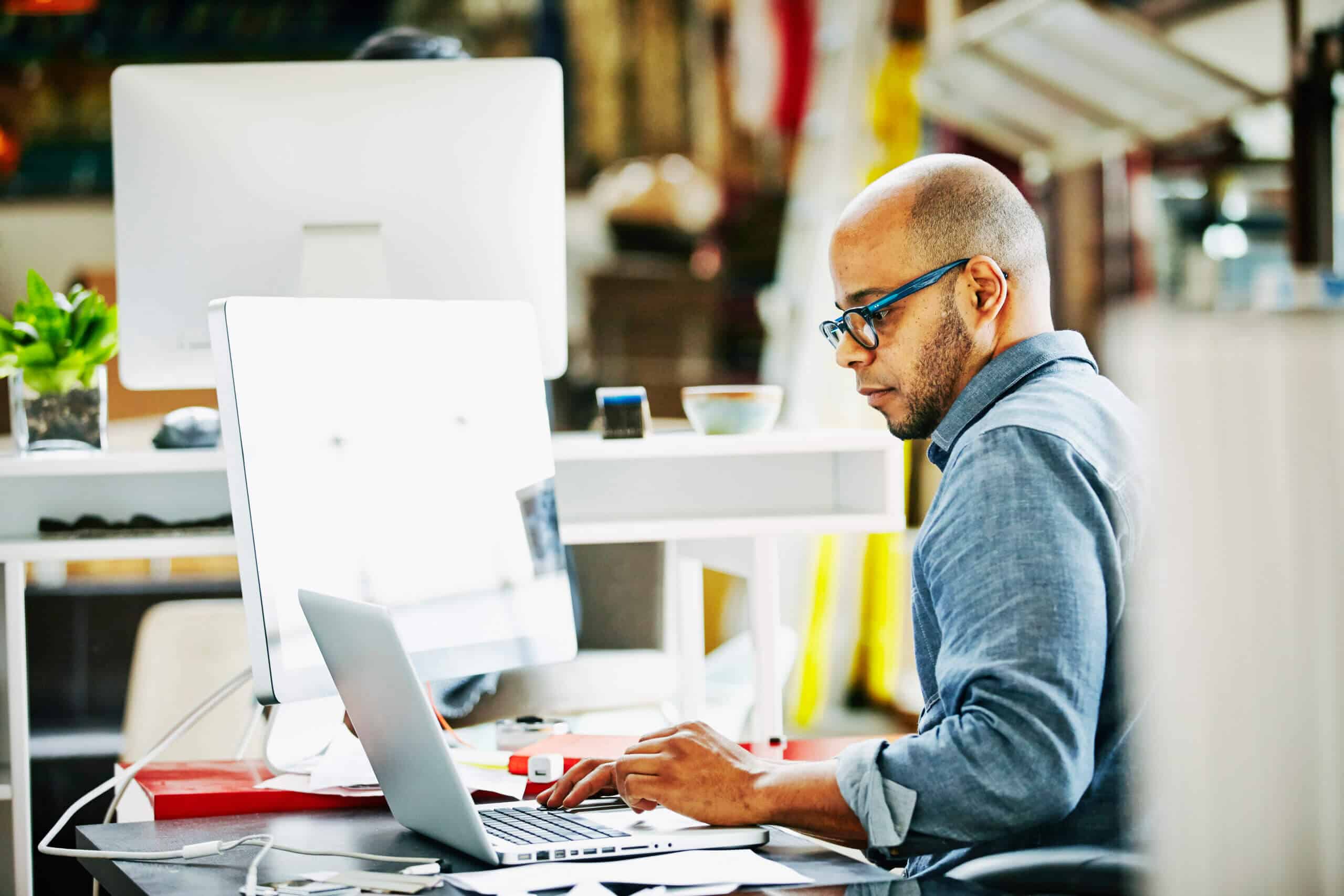 Businessman sitting at workstation in startup office working on project on laptop