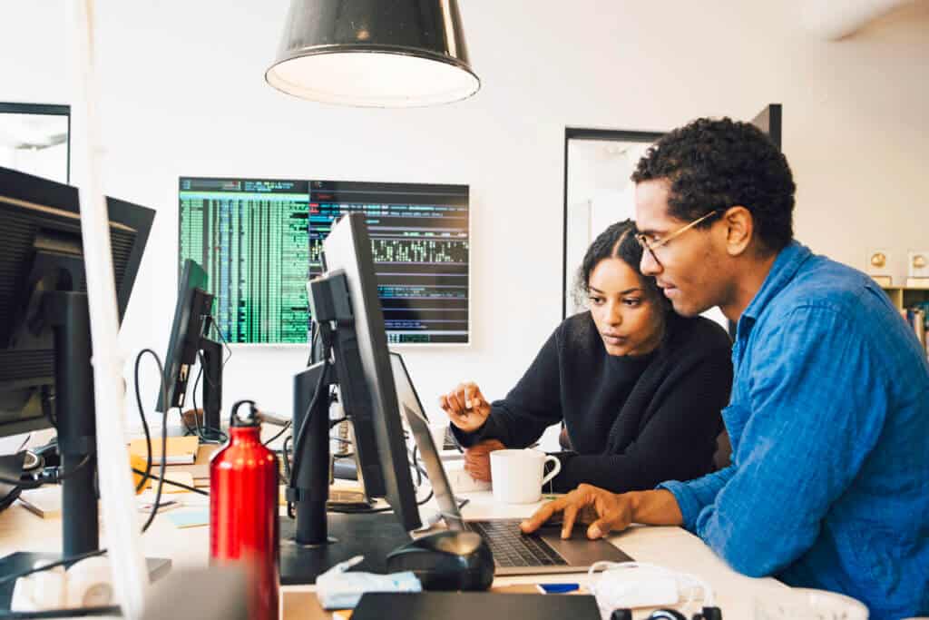 Focused male and female engineers coding over laptop on desk in office Focused male and female engineers coding over laptop on desk in office