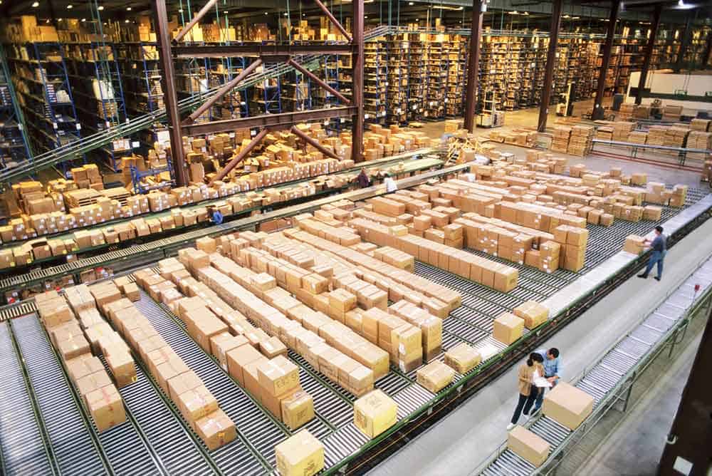 Overview of a large industrial distribution warehouse storing products in cardboard boxes on conveyor belts and racks.