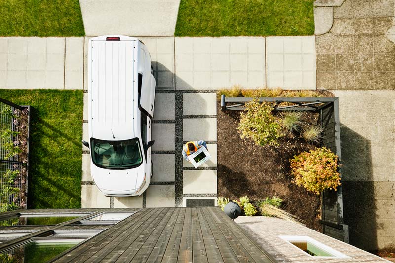 Overhead view of female delivery driving carrying produce box to front door of home