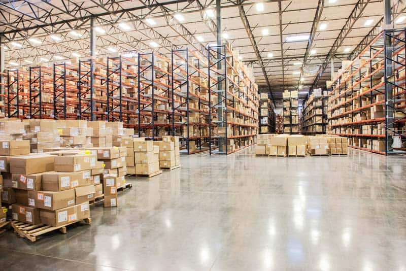 View down aisles of racks holding cardboard boxes of product on pallets in a large distribution warehouse