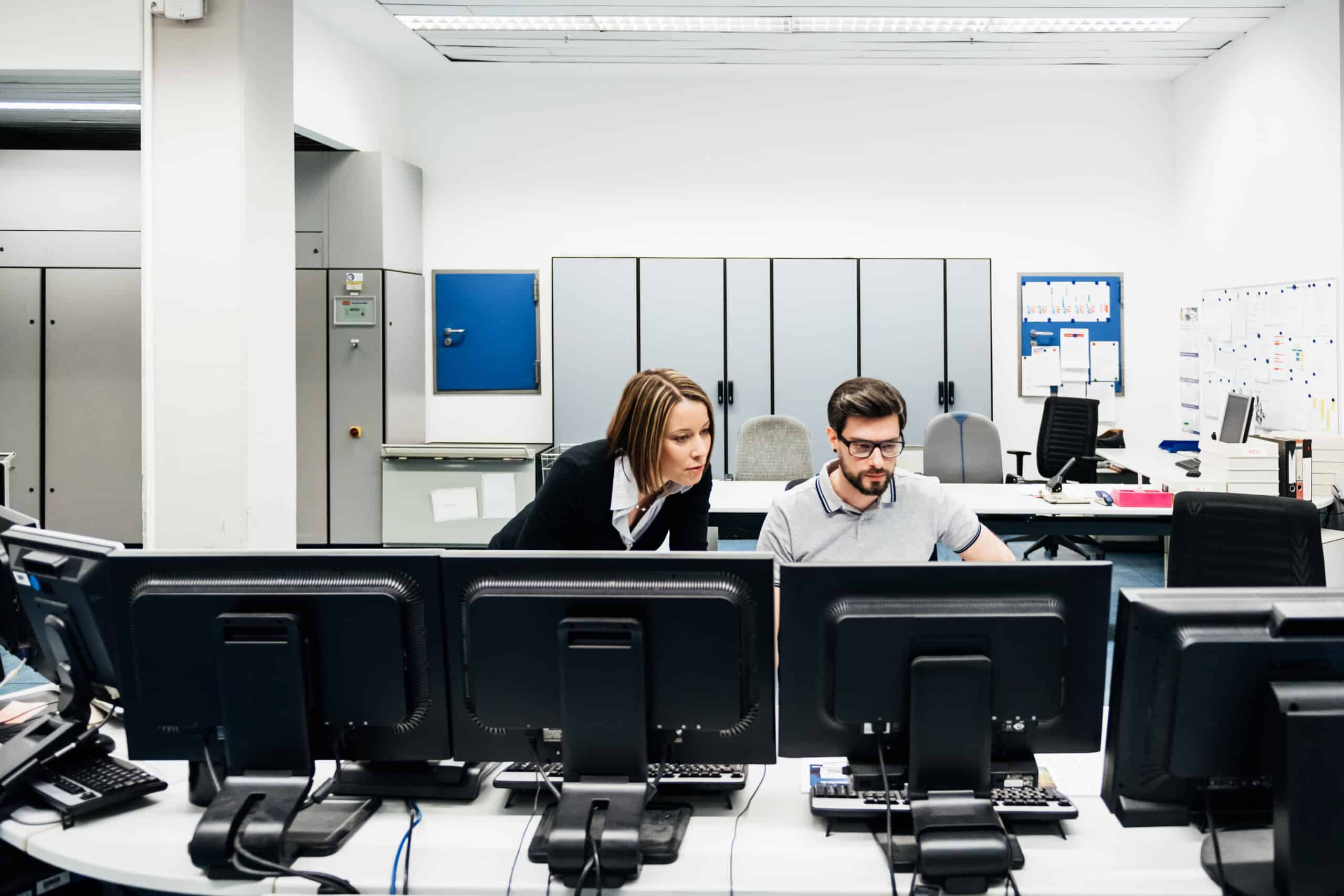 Operations Manager Assisting Colleague In Factory Control Room